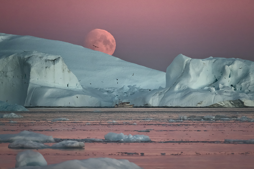 HUGE MOON PEEKING FROM BEHIND A LARGE ICEBERD IN ILULISSAT FJORD, GREENLAND